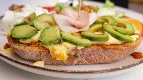 Open faced sandwich featuring toasted bread topped with avocado, melted cheese, Stock Footage 338219996