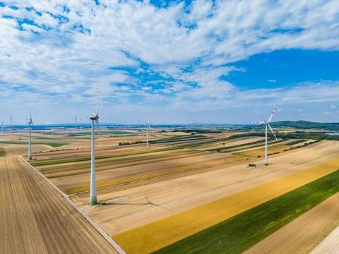 In an open field, several wind turbines rotate steadily under a blue sky. The Stock Photos