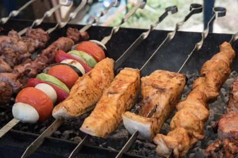 On an open fire, in the grill, preparing red fish, vegetables, meat. Stock Photos