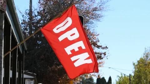 Open flag, in red and white, waving in the wind outside a store near a set of Stock Footage 107349165