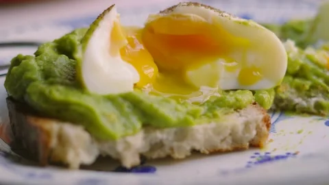 Open Fresh Soft Boiled Eggs with Golden Yolk with Smashed Avocado on Sourdough Stock Footage 341605479