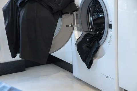 Open front load washing machine with black laundry hanging out Stock Photos