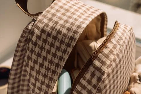 Open gingham backpack filled with school supplies in warm natural sunlight Stock Photos