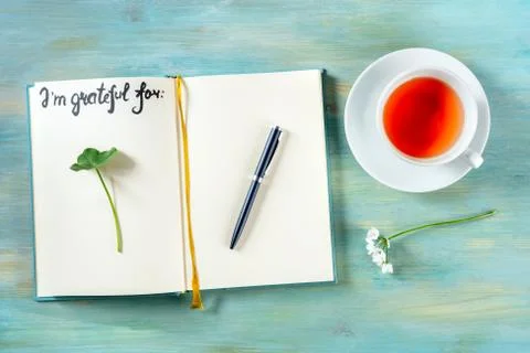 Open gratitude journal with a pen and a cup of tea, with the handwritten phrase Stock Photos