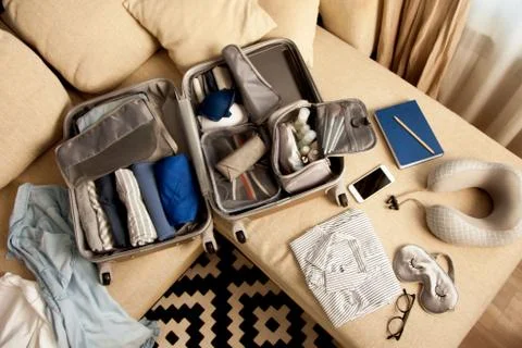 Open grey suitcase with different clothes packed for journey at home. Nordic Stock Photos