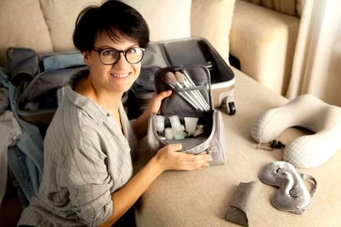 Open grey suitcase with different clothes and cosmetics packed for journey at Stock Photos