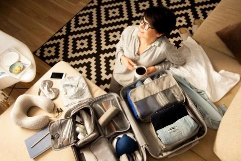 Open grey suitcase with different clothes packed for journey at home. Nordic Stock Photos