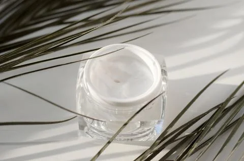 An open jar of cream on a light background with palm twigs. Skin care concept Stock Photos