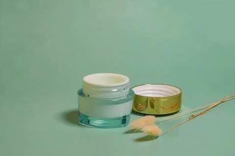 An open jar of face cream, dried lagurus flowers on a colored background Stock Photos