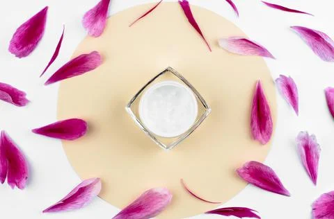 An open jar of moisturizer on a round beige background with pink petals Stock Photos