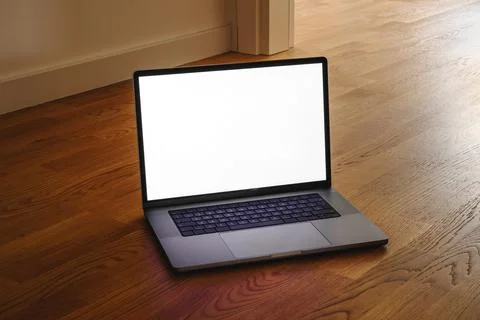 Open laptop with blank white screen placed on wooden floor in warm interior.. Stock Photos