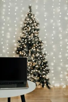 An open laptop is on the table against the backdrop of the Christmas tree Stock Photos