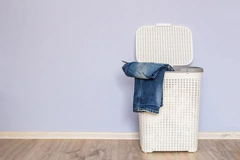 An open laundry basket with jeans inside on the floor against the blue wall Stock Photos