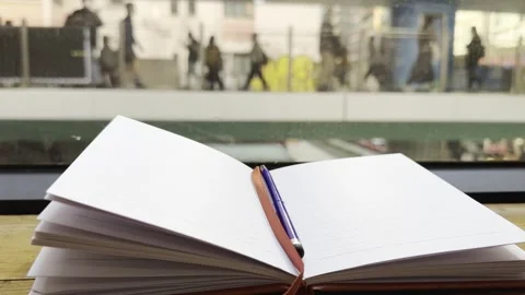 Open lined notebook with pen placed on windowsill, blurred urban street Stock Footage 297717242