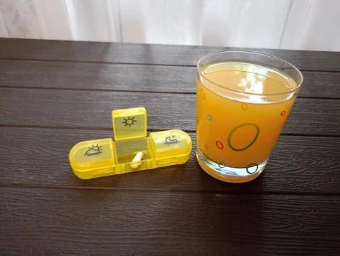 An open medication container with a white iron capsule and a glass of juice.. Stock Photos