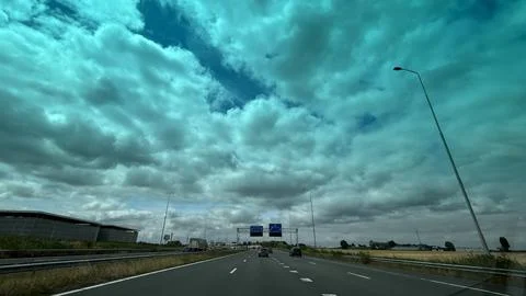 Open motorway under dramatic cloudy sky with distant traffic and road signs 库存照片