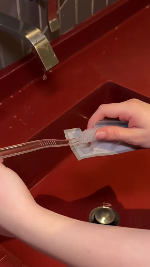 To open a new toothbrush in a hotel to brush teeth over the sink water dripping Stock Footage 314367366