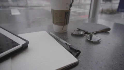 Open notebook and coffee in front of a window on a rainy day Stock Footage 157499255