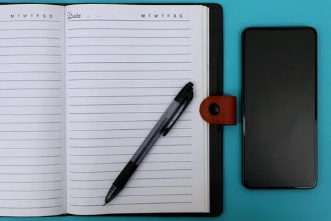 An open notebook with a ballpoint pen on it and a smartphone next to it on .. Stock Photos