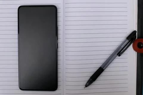 An open notebook with a ballpoint pen on it and a smartphone next to it on .. Stock Photos