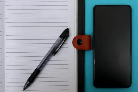 An open notebook with a ballpoint pen on it and a smartphone next to it on .. Stock Photos