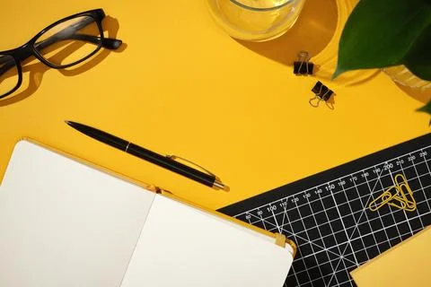 Open notebook with black pen on bright yellow desk. Glasses, binder clips, pa Stock Photos