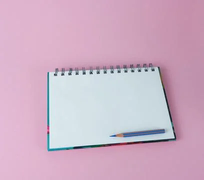 An open notebook with a blue pencil on a pink background. Stock Photos