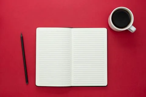 Open notebook with coffee cup on red background. Stock Photos
