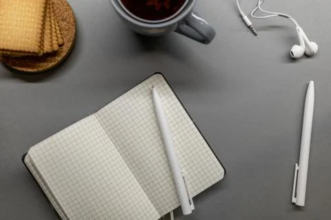 Open notebook cup cookie and pens on grey table Stock Photos