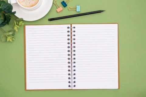 Open notebook with empty page and coffee cup. Table top, work space on green  Stock Photos