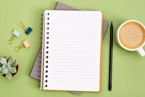 Open notebook with empty page and coffee cup. Table top, work space on green  Stock Photos
