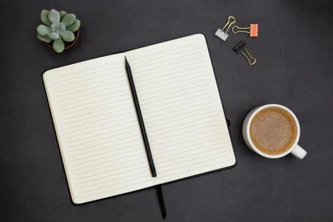 Open notebook with empty page and coffee cup. Table top, work space on dark b Stock-Fotos