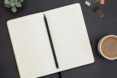 Open notebook with empty page and coffee cup. Table top, work space on dark b Stock Photos