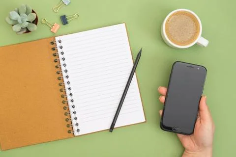 Open notebook with empty page, pencil, coffee cup and hand holding a smartpho Stock-Fotos