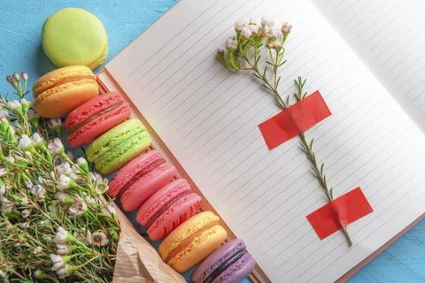 Open notebook with flower stuck on it, multicolored macaroons and tiny white Foto stock