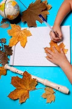 Open notebook, flute, globe, autumn leaves and hands of Caucasian girl Stock Photos