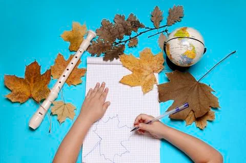 Open notebook, flute, globe, autumn leaves and hands of Caucasian girl Stock Photos