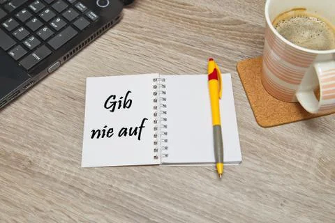 Open notebook with German text "Gib Nie Auf" (Never Give Up) and a cup of coffee Stock Photos