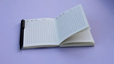 An open notebook with a grid pattern and a black pen lies beside it Stock Footage 331790210