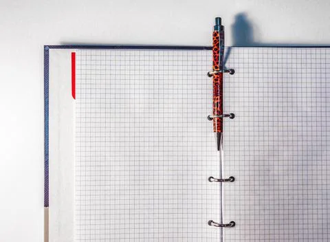 Open notebook with inserted orange ballpoint pen on a white table copyspace Stock Photos