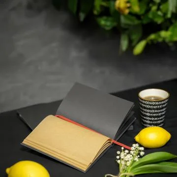 Open notebook, lemons, a cup of tea, lilies of the valley on a black backgr.. Foto stock