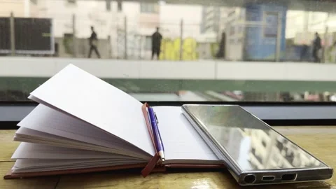 Open notebook with pen and smartphone placed on wooden surface by window Video stock 297717238