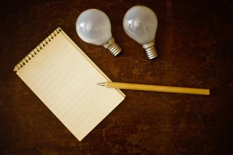 Open notebook with pen and two light bulbs on a wooden table. Flatlay. Idea o Stock Photos