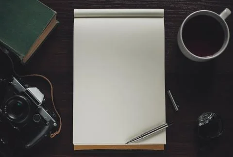Open notebook, pen, cup of tea, book, retro camera on table, top view Stock Photos