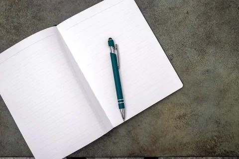 An open notebook with a pen lies on a dark textured surface. Stock Photos