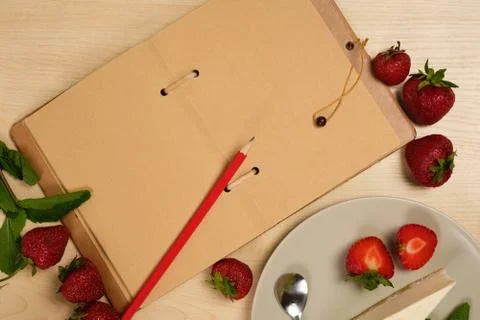 An open notebook with a red pencil is surrounded by strawberries and a plate Stock Photos