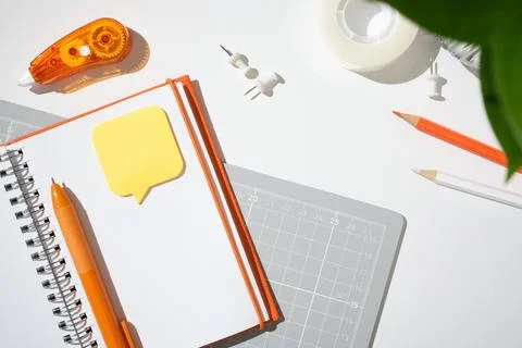 Open notebook with sticky note, orange correction tape, and cutting mat on .. 스톡 사진