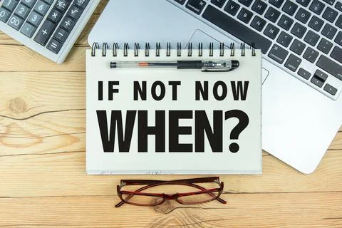 Open notebook with text "If Not Now When?" and a laptop on wooden background. Stock Photos