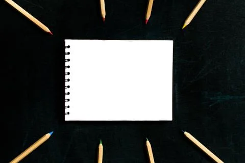 Open notepad and open multicolored pencils on a black board background. Place Stock Photos