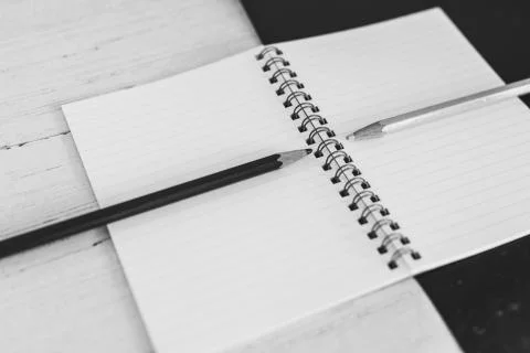 Open notepad on black and white background with pencils of the opposite color Stock Photos